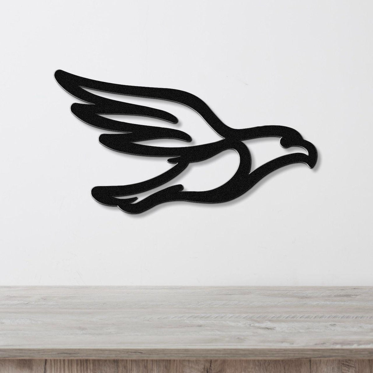 Black metal eagle wall art with a bold silhouette and wing cutouts, mounted on a white wall above a light wood surface.