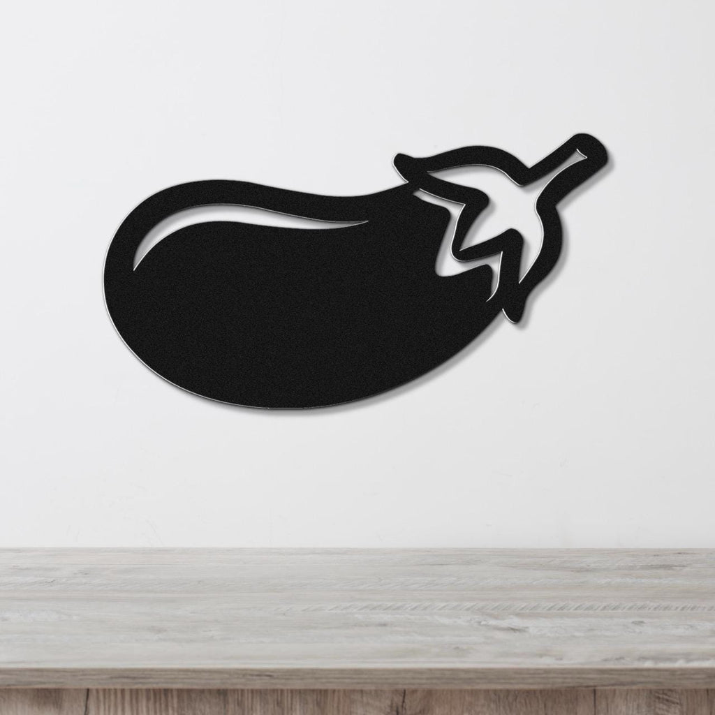 Black metal eggplant wall art with a cutout stem and leaf, mounted on a white wall above a light wood countertop.