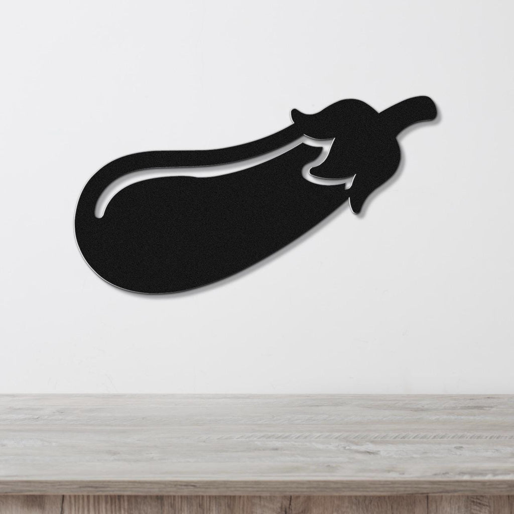 Black metal eggplant wall sculpture with a cutout stem and leaf detail, mounted on a white wall above a light wood countertop.