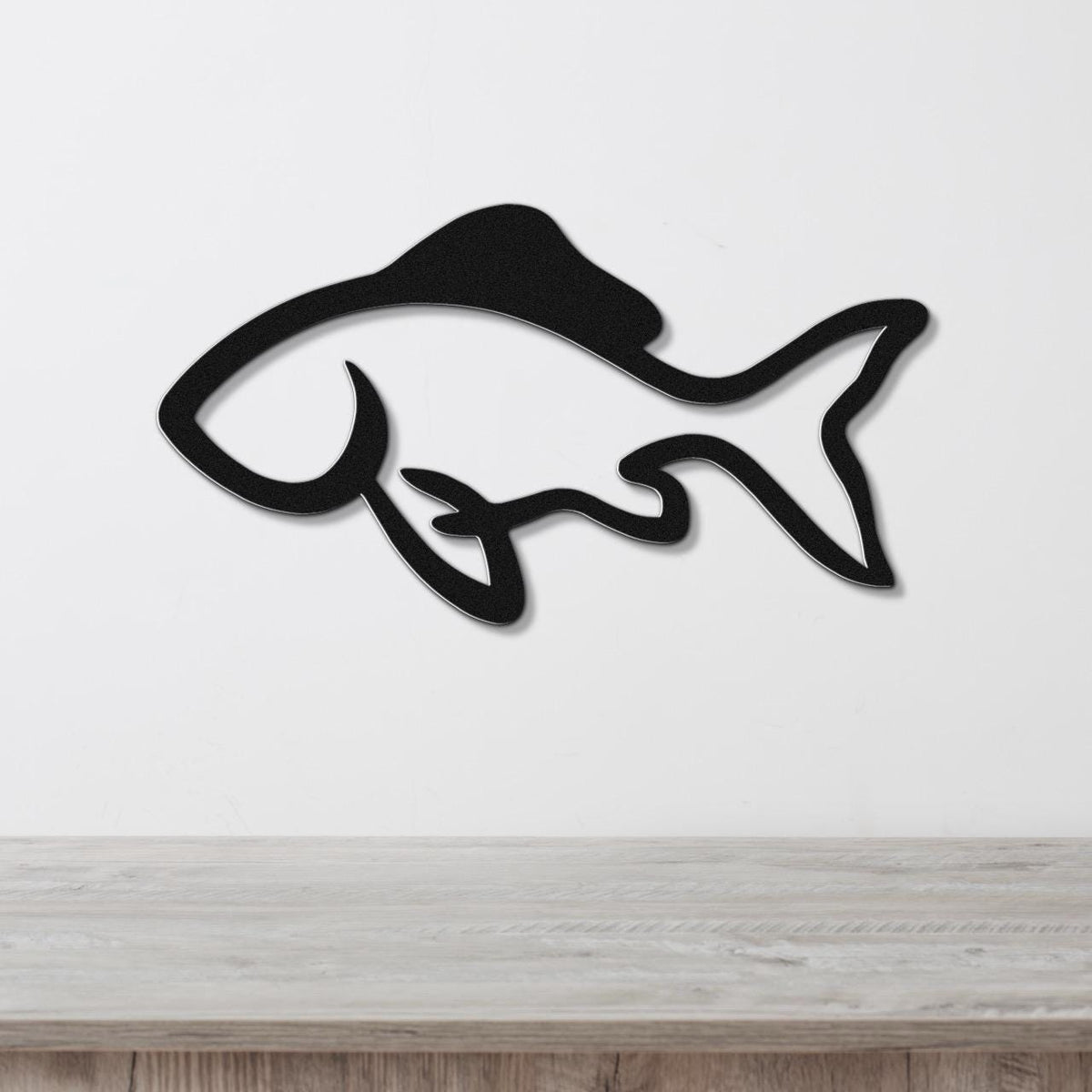 Black metal fish wall art with a sleek silhouette design, mounted on a white wall above a light wood surface.
