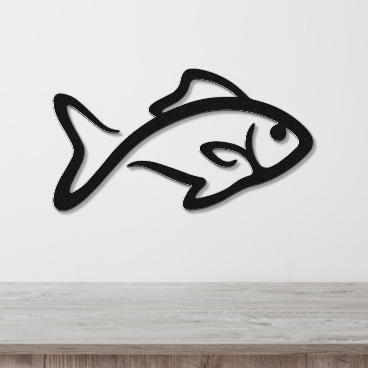 Black metal fish wall art with a silhouette design, mounted on a white wall above a light wood surface.