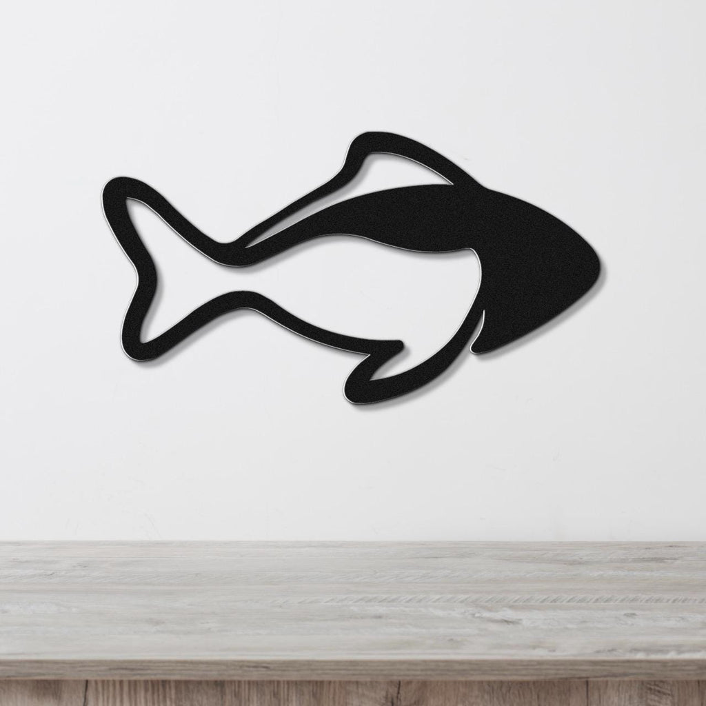 Black metal fish wall art with bold line silhouette cutout, mounted on a white wall above a light wood surface.