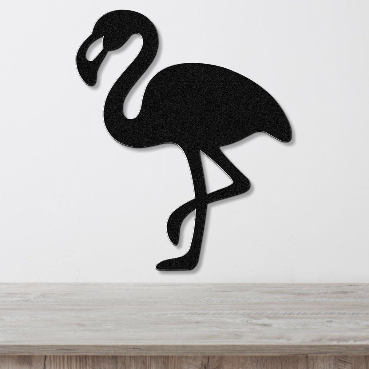 Black metal flamingo wall art silhouette with cutout details, mounted on a white wall above a light wood counter.