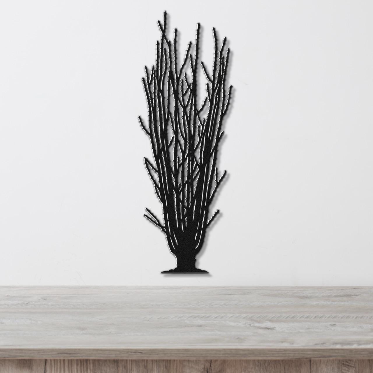 Black metal wall art cutout of a tall ocotillo plant with branching stems, mounted on a white wall above a light wood surface.