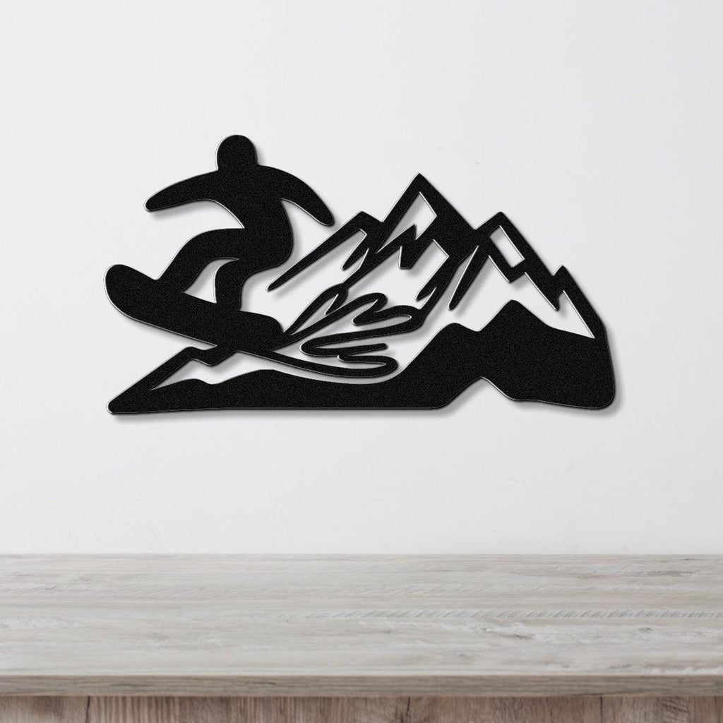 Black metal wall art featuring a snowboarder silhouette and mountain range with powder-spray cutouts, mounted on a white wall above a wooden counter.