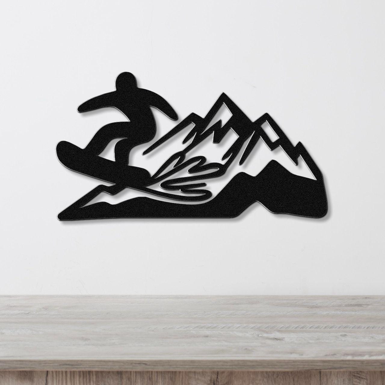 Black metal wall art featuring a snowboarder silhouette and mountain range with powder-spray cutouts, mounted on a white wall above a wooden counter.