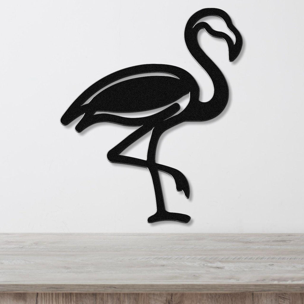 Black metal flamingo wall art with a silhouette cutout design, mounted on a white wall above a light wood surface.