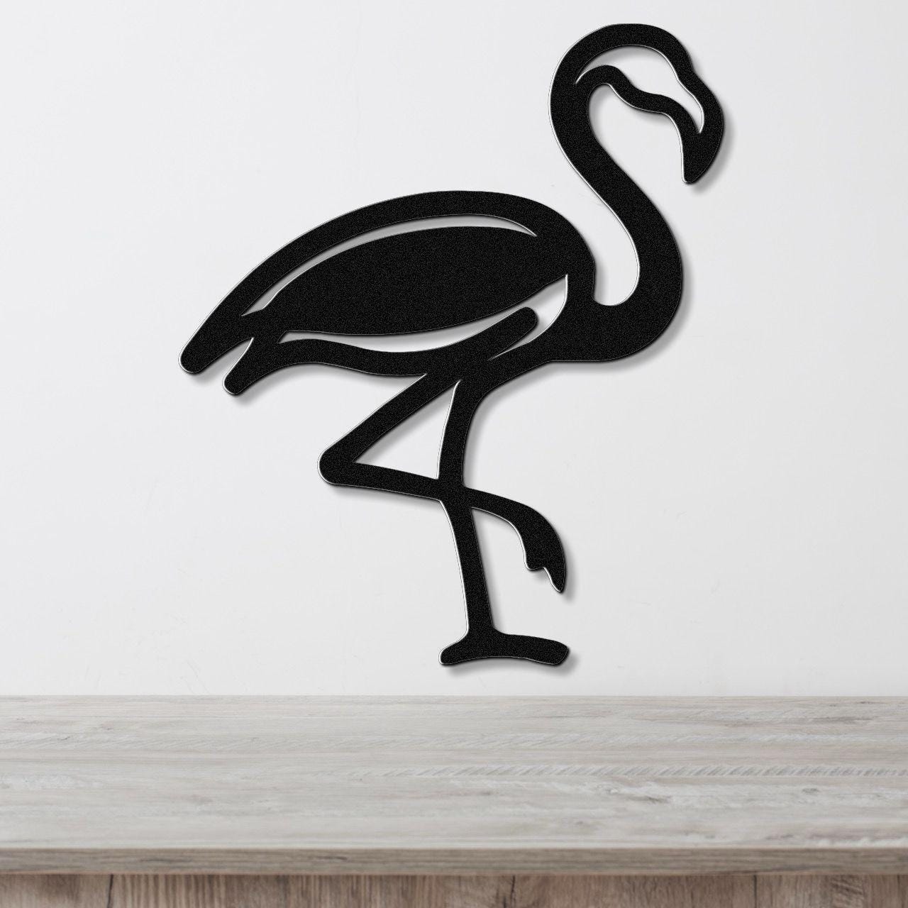 Black metal flamingo wall art with a silhouette cutout design, mounted on a white wall above a light wood surface.