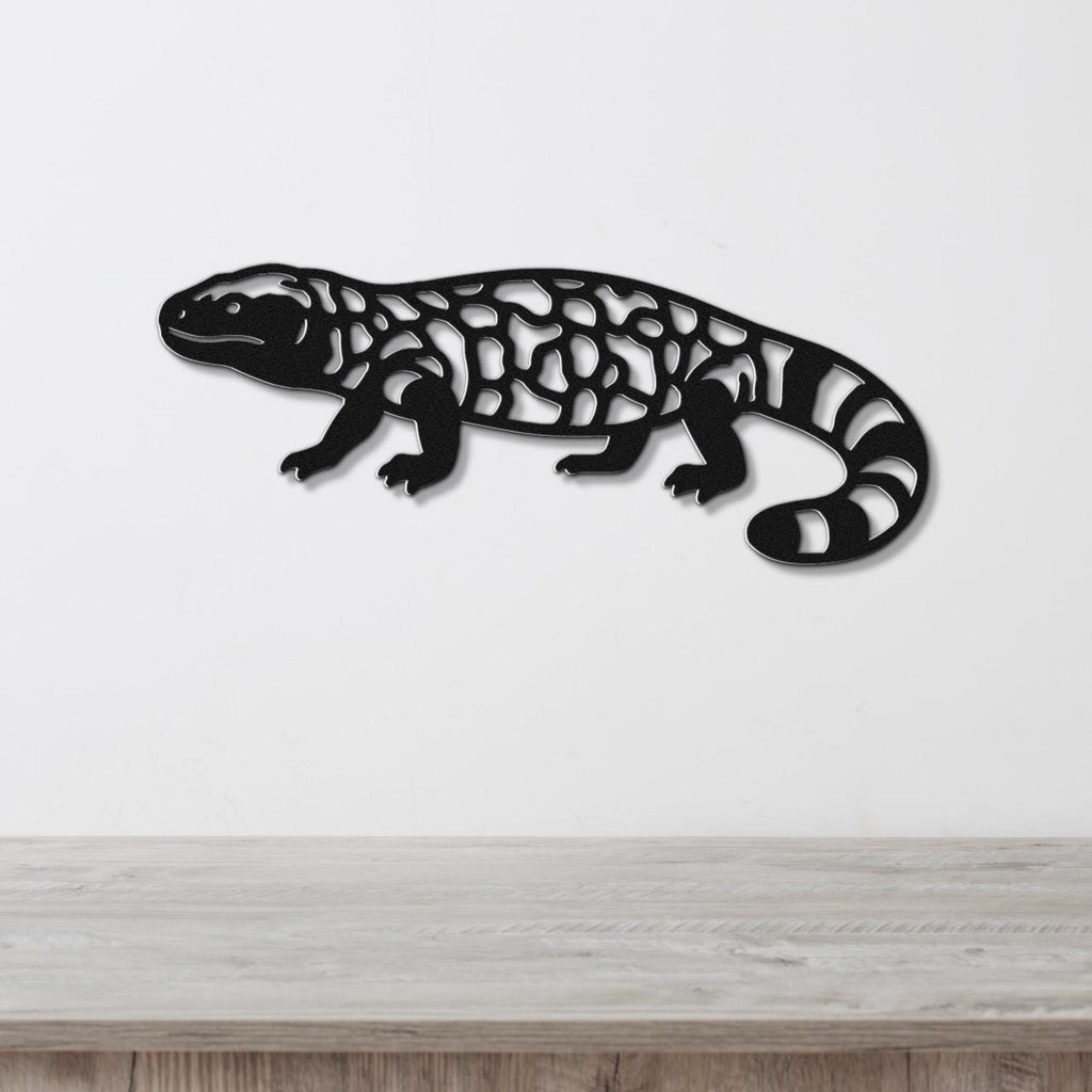 Black metal wall art of a Gila monster with intricate cutout patterns, mounted on a white wall above a wooden surface.