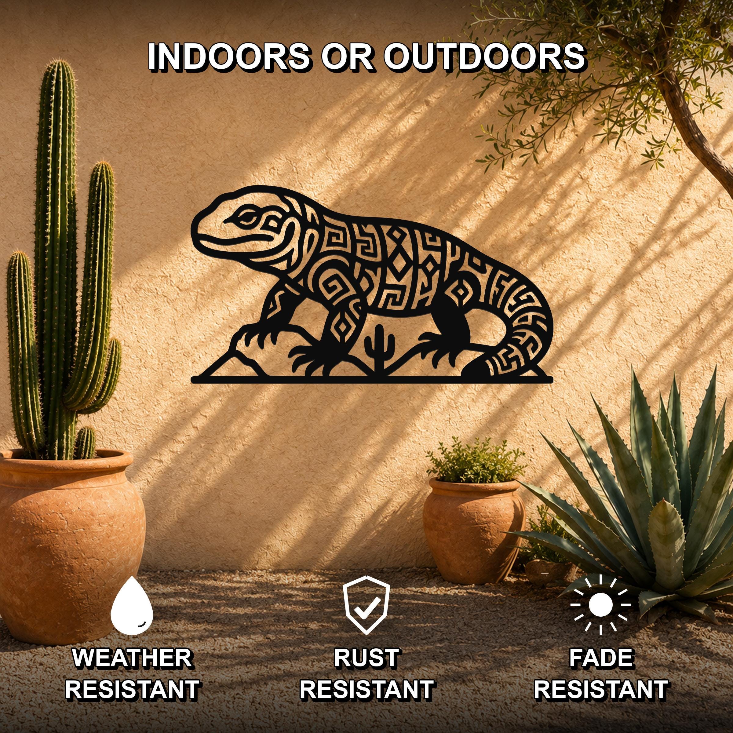 Black metal Gila monster wall art with intricate geometric cutouts, mounted on an outdoor stucco wall beside potted cacti and succulents.