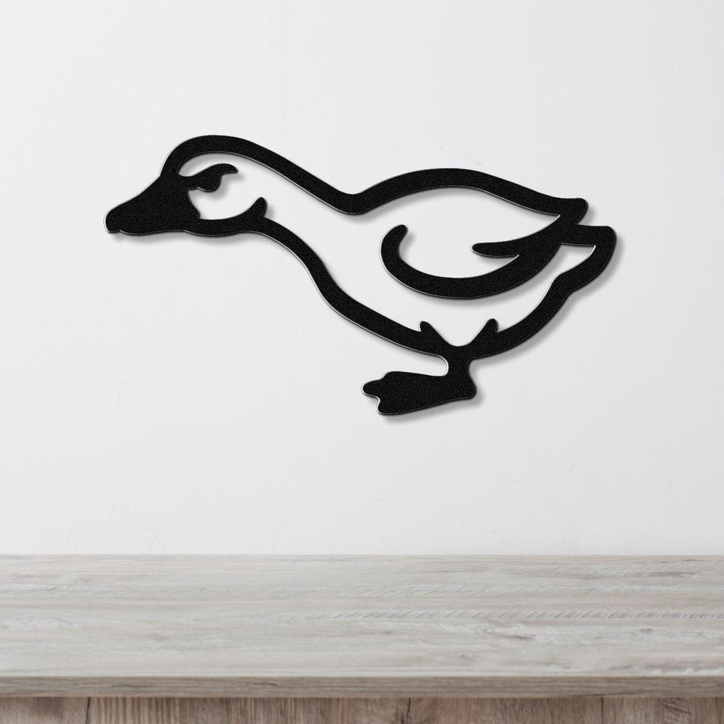Black metal goose wall art silhouette with cutout details, mounted on a white wall above a light wood surface.