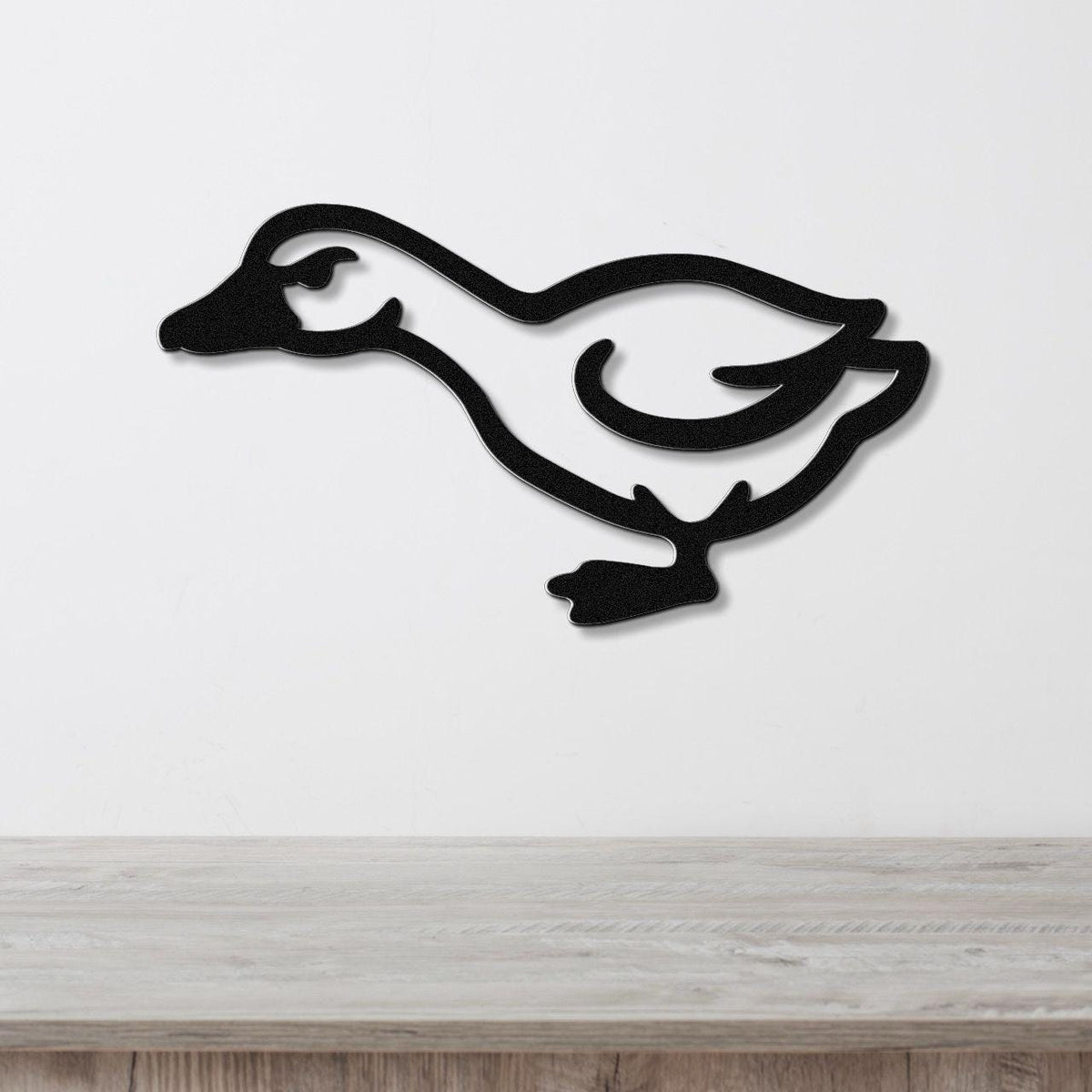 Black metal goose wall art silhouette with cutout details, mounted on a white wall above a light wood surface.