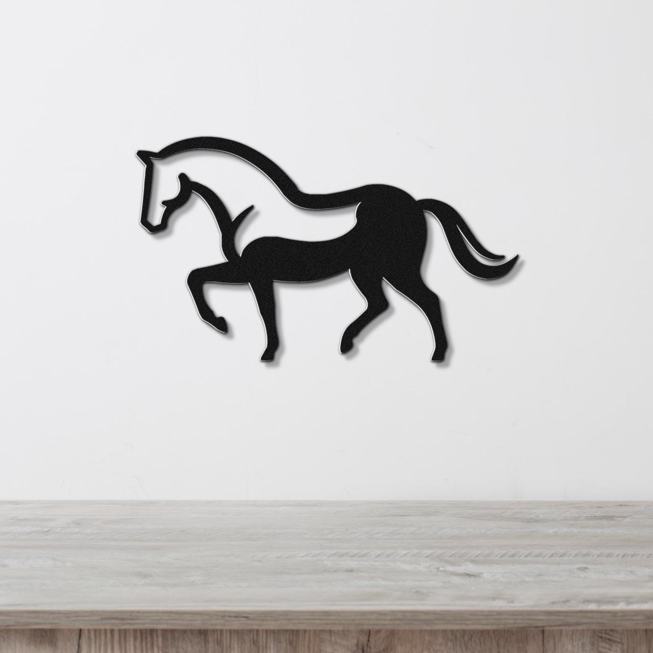 Black metal horse wall art with a silhouette design, mounted on a white wall above a wooden surface.