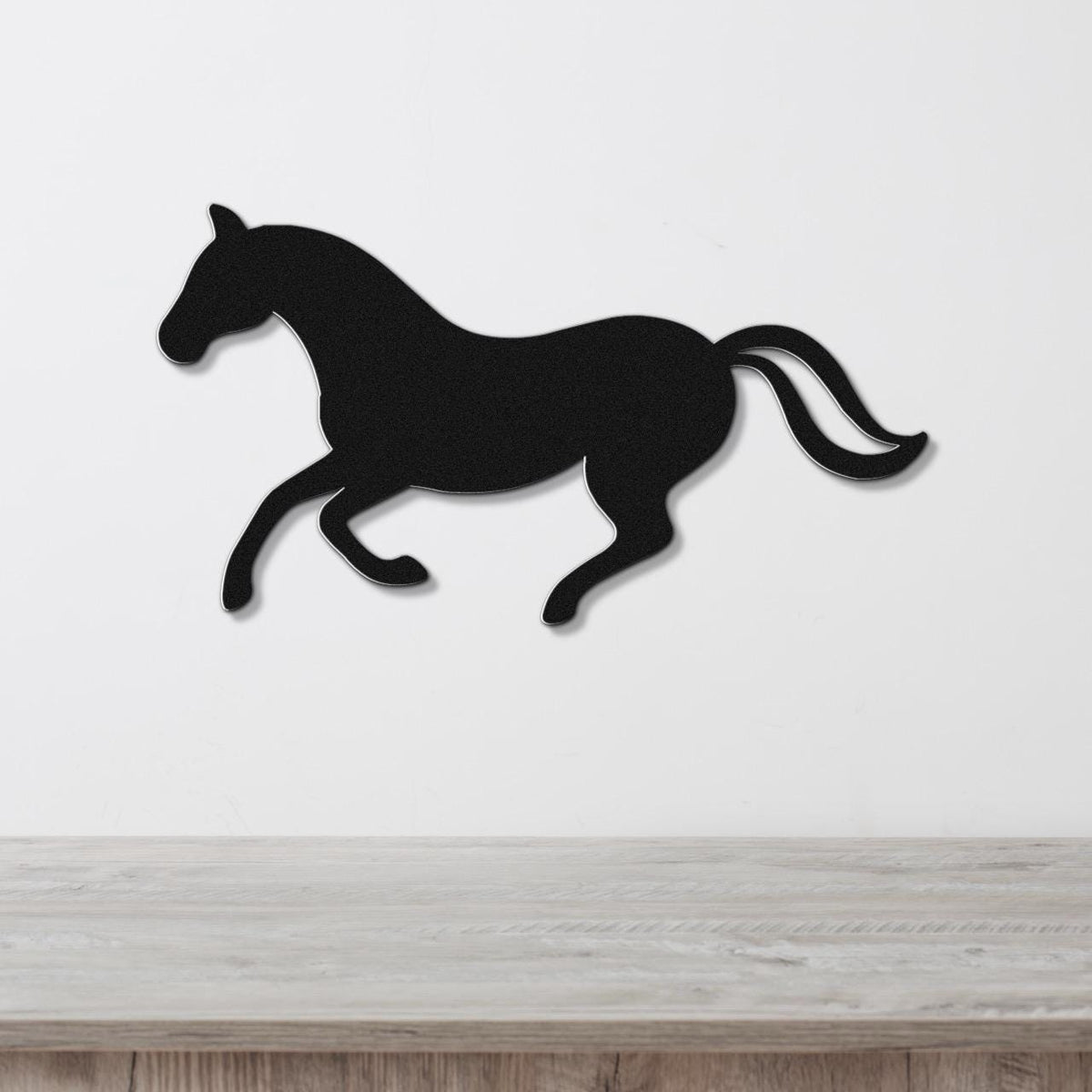 Black metal horse wall art silhouette in a running pose, mounted on a white wall above a light wood surface.