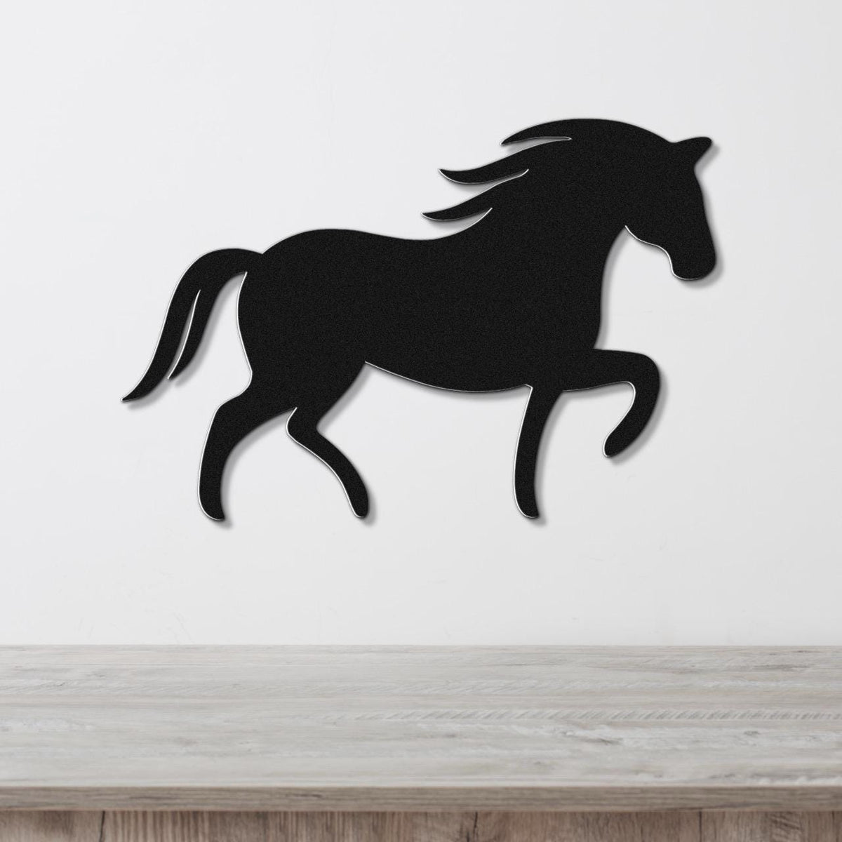 Black metal horse wall art silhouette with flowing mane and tail, mounted on a white wall above a light wood surface.