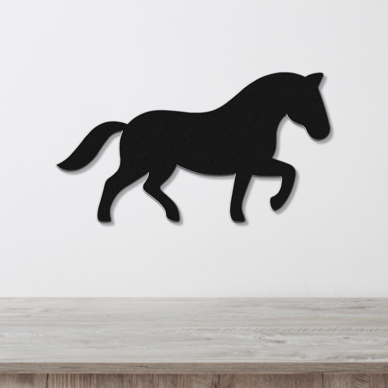 Black metal horse wall art silhouette in a walking pose, mounted on a white wall above a light wood surface.
