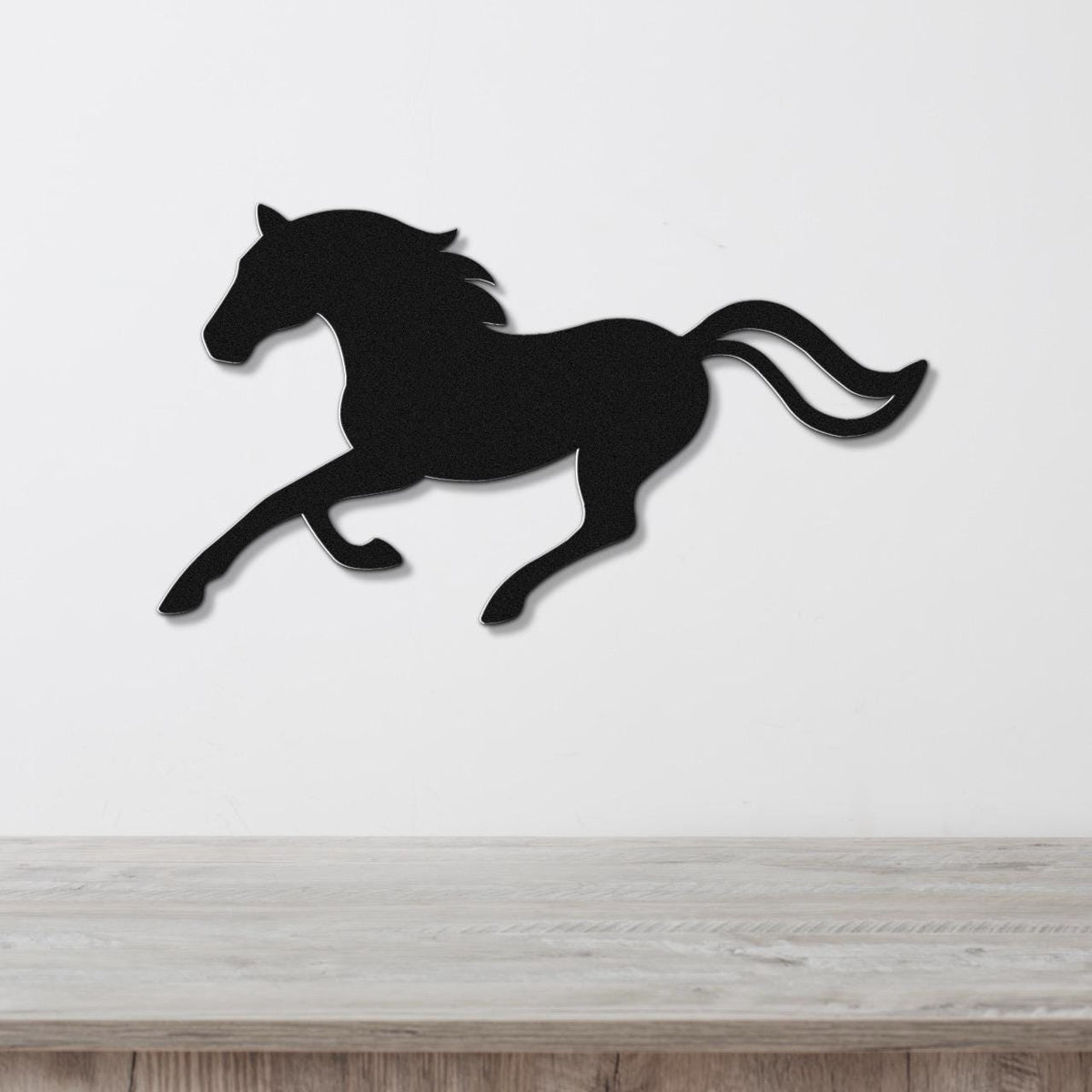 Black metal horse wall art silhouette in a running pose, mounted on a white wall above a light wood surface.