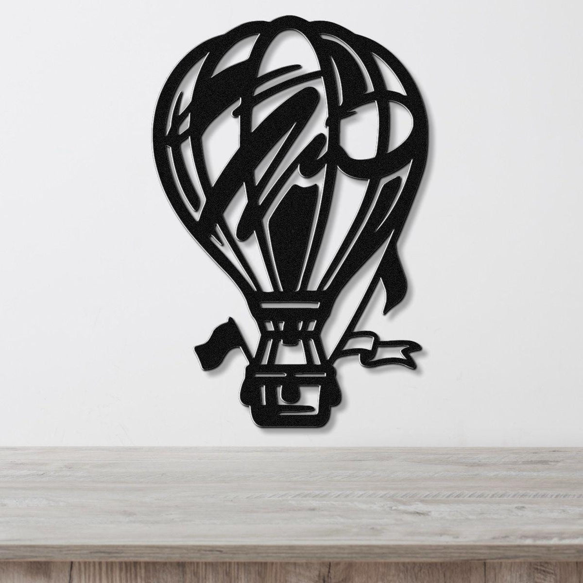 Black metal hot air balloon wall art with internal cutout details, mounted on a white wall above a light wood surface.
