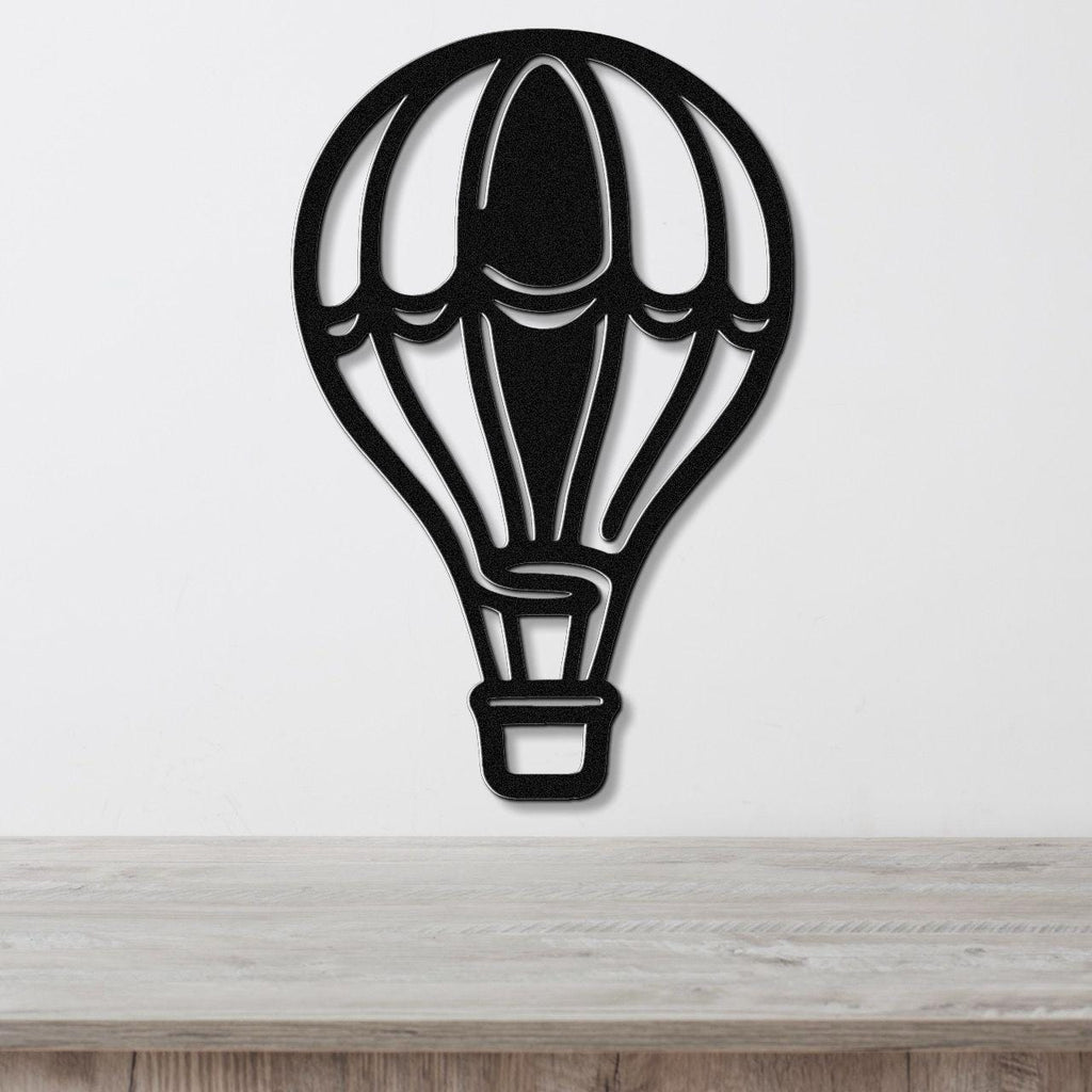 Black metal hot air balloon wall art with internal cutout details, mounted on a white wall above a light wood surface.