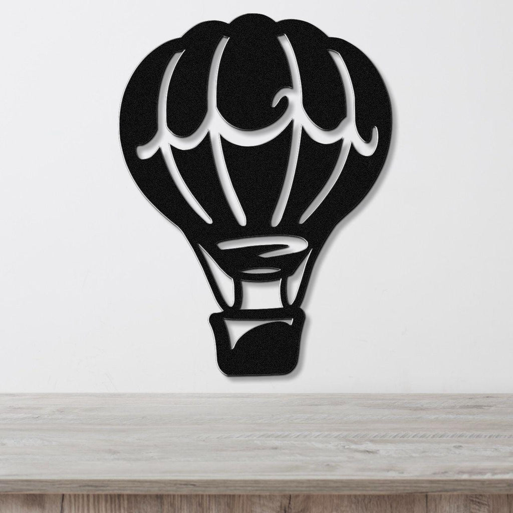 Black metal wall art in the silhouette of a hot air balloon with internal cutout details, mounted on a white wall above a light wood surface.