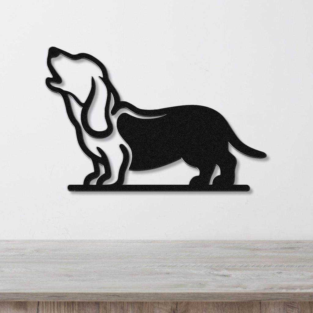 Black metal wall art silhouette of a basset hound howling, mounted on a white wall above a light wood surface.
