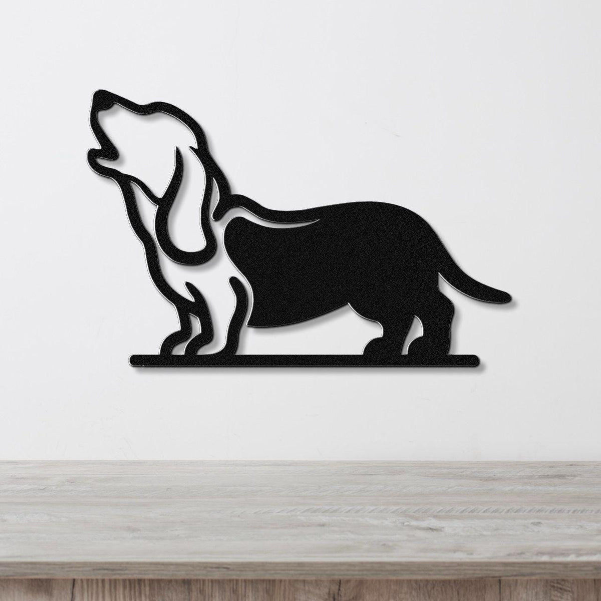 Black metal wall art silhouette of a basset hound howling, mounted on a white wall above a light wood surface.