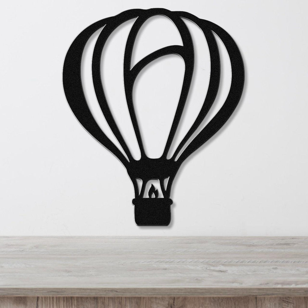 Black metal wall art in the silhouette of a hot air balloon with internal cutout details, mounted on a white wall above a light wood surface.