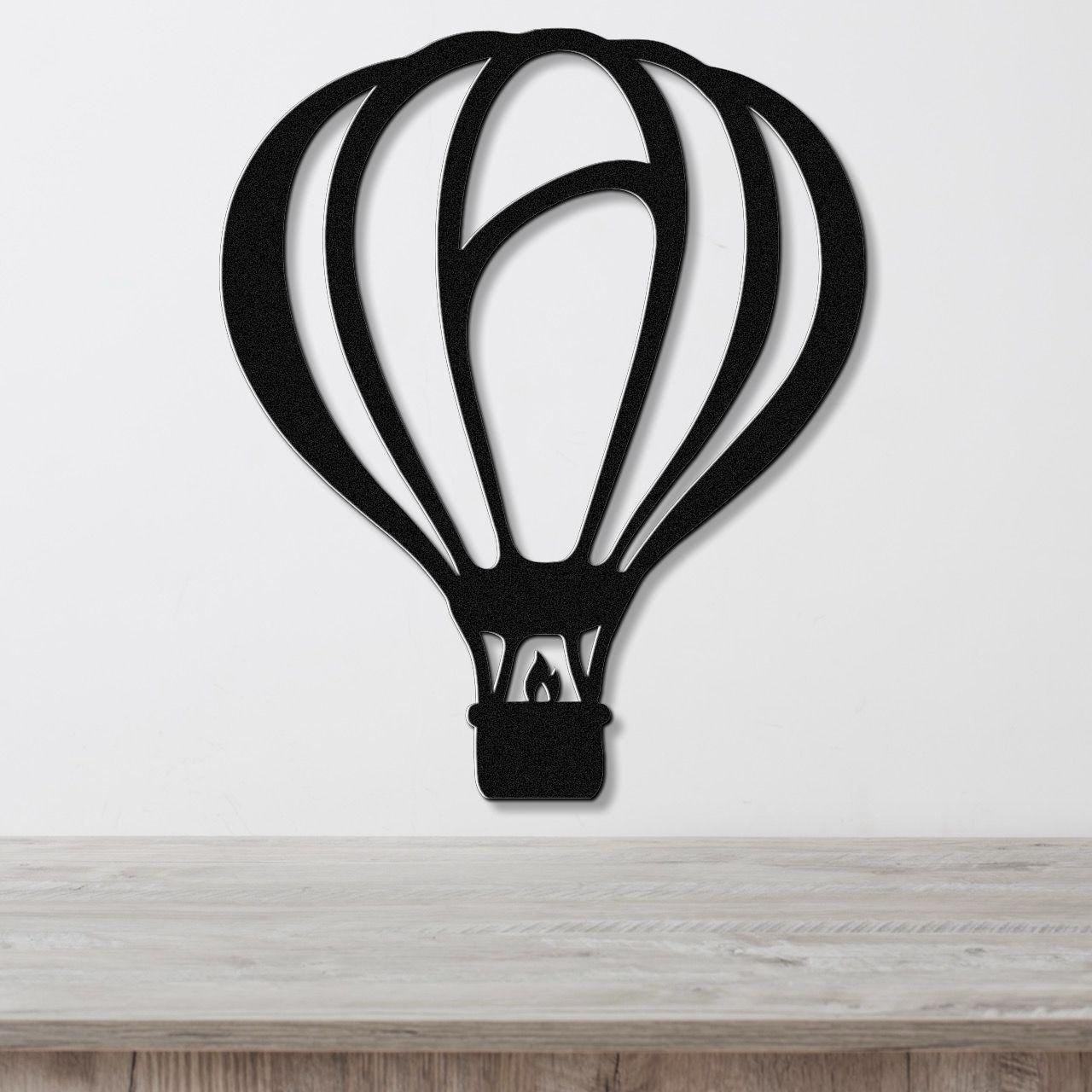 Black metal wall art in the silhouette of a hot air balloon with internal cutout details, mounted on a white wall above a light wood surface.