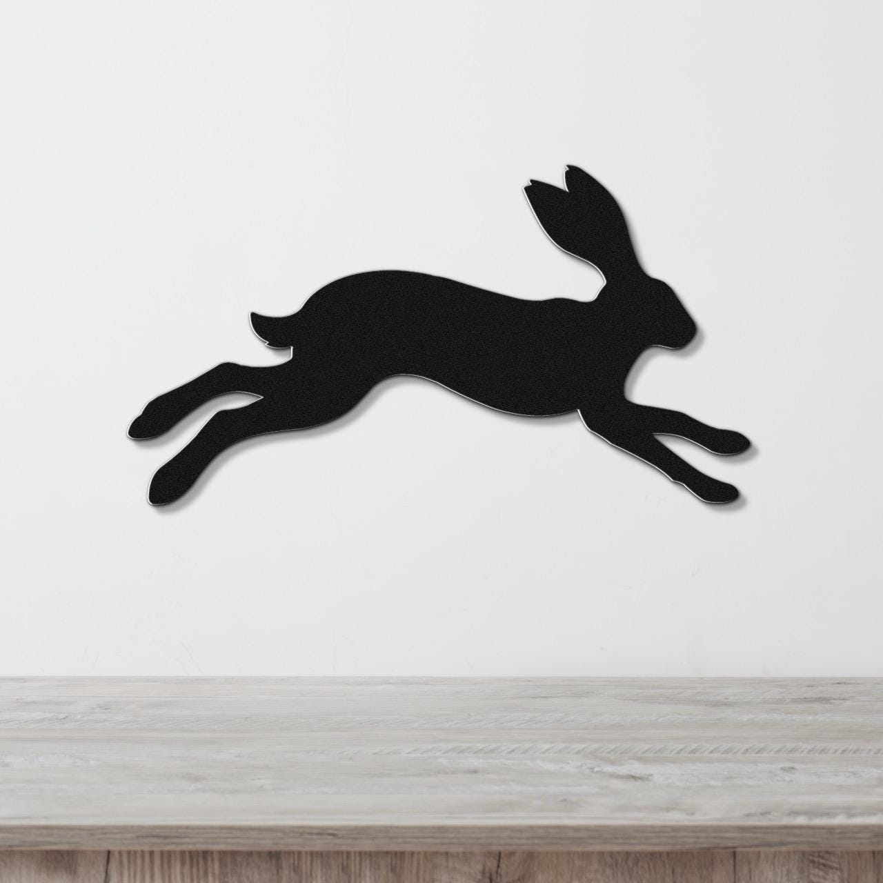 Black metal jackrabbit wall art in a leaping silhouette, mounted on a white wall above a light wood counter.