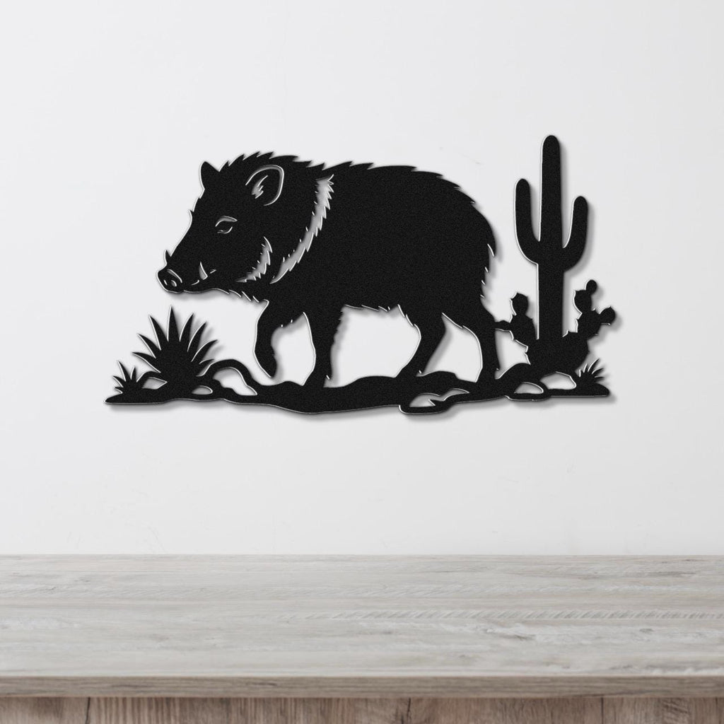 Black metal wall art featuring a javelina silhouette with cactus and desert plants, mounted on a white wall above a wooden surface.