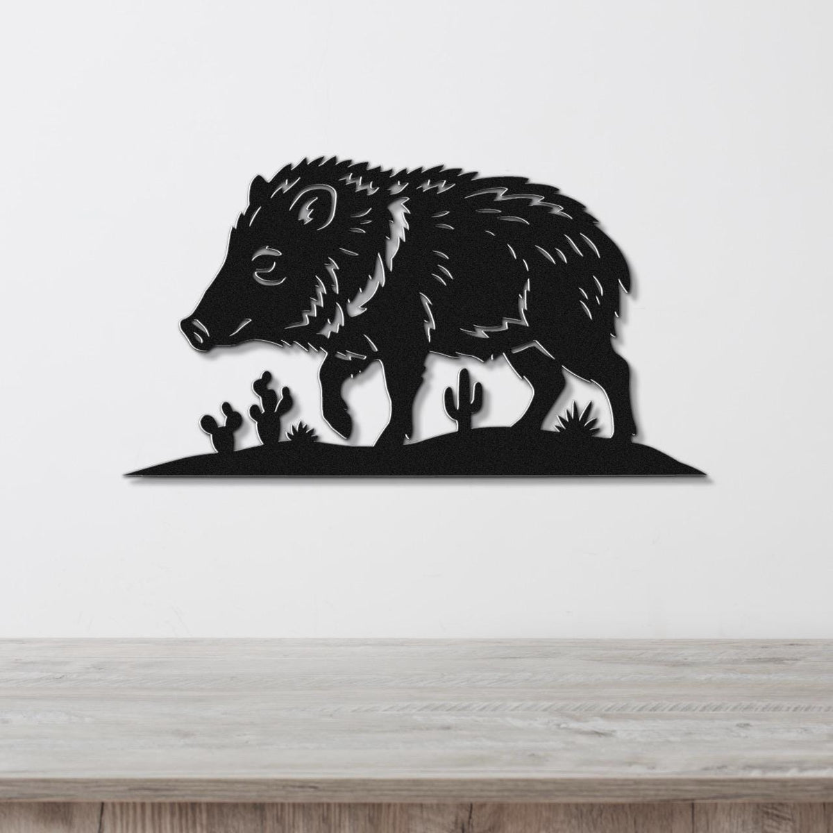 Black metal wall art silhouette of a javelina with cactus cutouts, mounted on a white wall above a wooden surface.