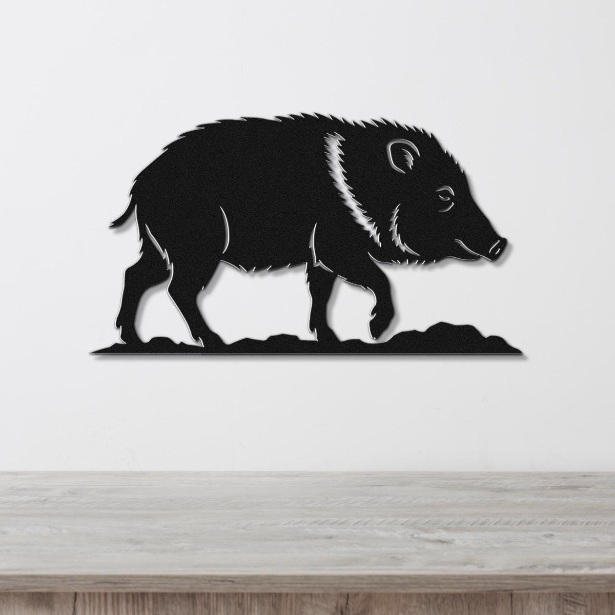 Black metal wall art silhouette of a javelina with detailed fur and facial features, mounted on a white wall above a wooden surface.
