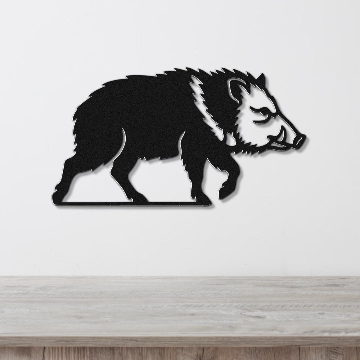 Black metal javelina wall art with a silhouette cutout design, mounted on a white wall above a light wood surface.