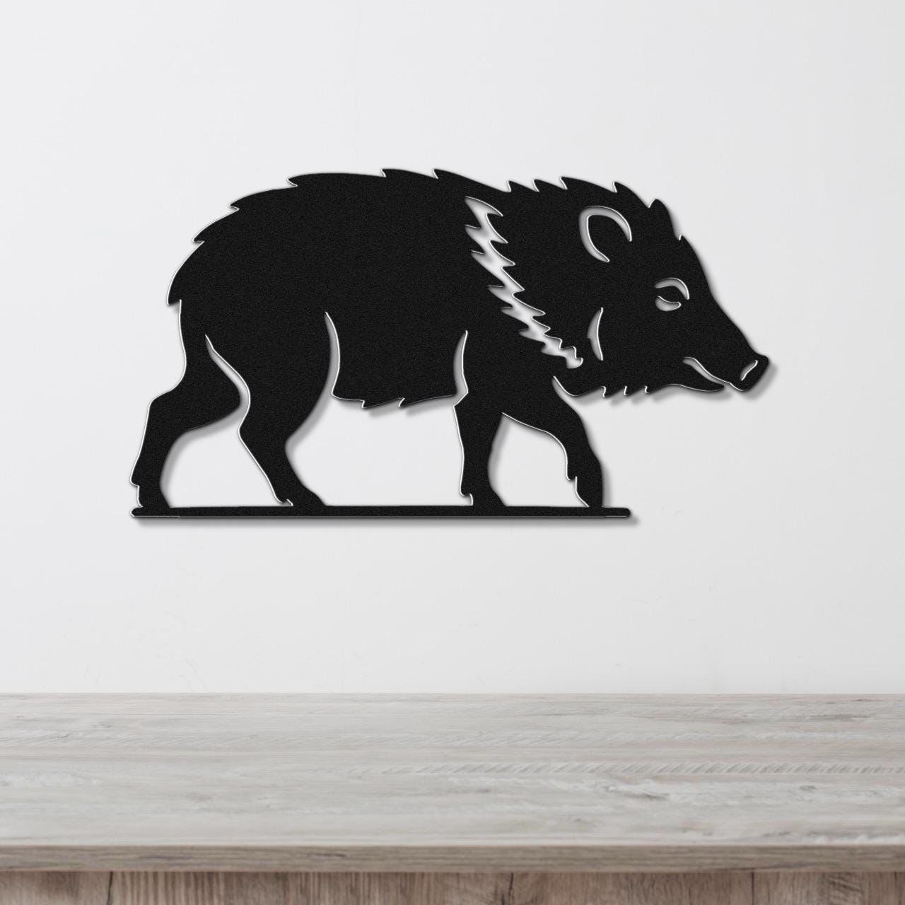 Black metal wall art silhouette of a javelina with spiky mane cutout, mounted on a white wall above a light wood counter.