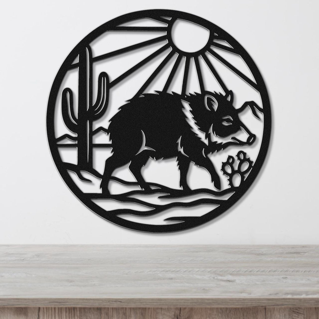 Black metal circular wall art featuring a javelina silhouette, cactus, sun rays, and paw prints, mounted on a white wall above a wooden surface.