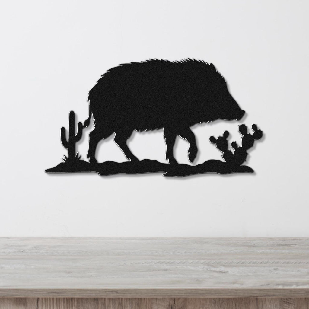 Black metal wall art silhouette of a javelina with cacti, mounted on a white wall above a wooden surface.