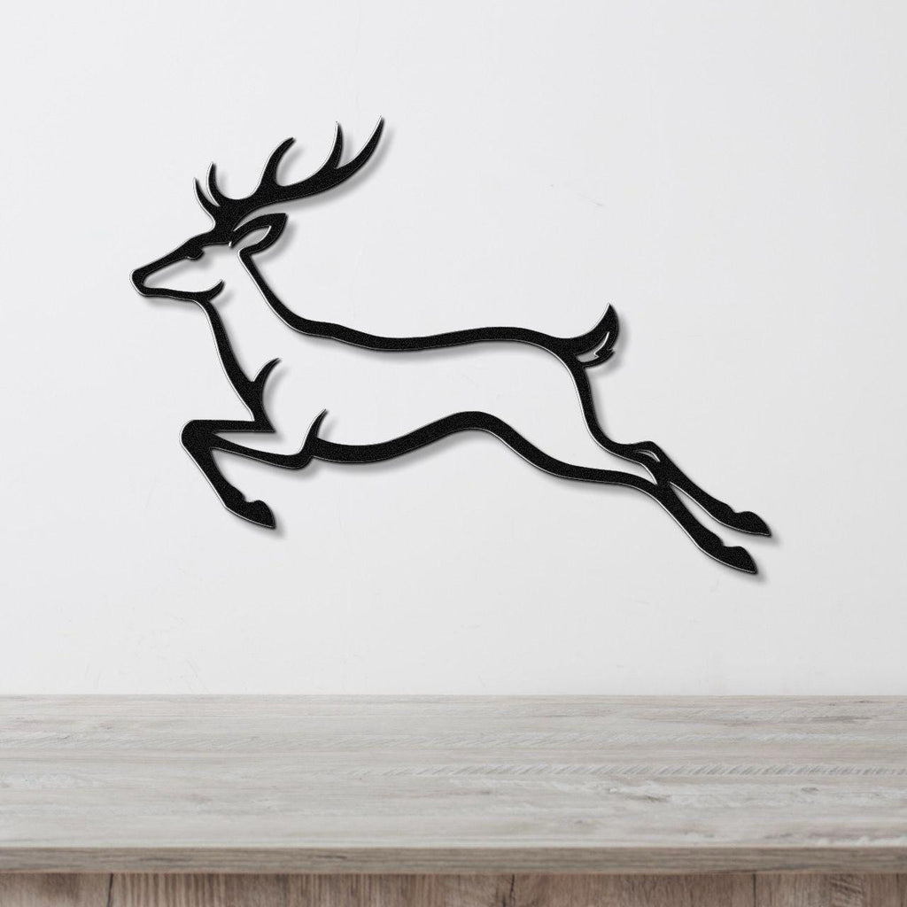 Black metal wall art of a leaping deer silhouette with antlers, mounted on a white wall above a light wood surface.