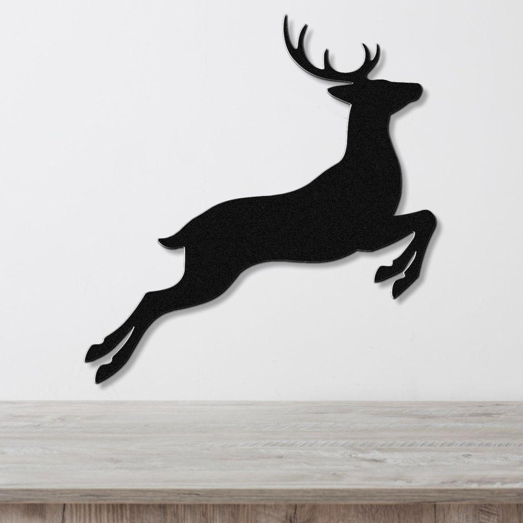 Black metal wall art of a jumping deer silhouette with antlers, mounted on a white wall above a light wood surface.