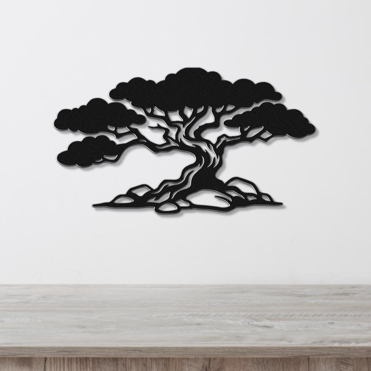 Black metal wall art in a wind-sculpted juniper tree silhouette with detailed branches and roots, mounted on a white wall above a light wood surface.