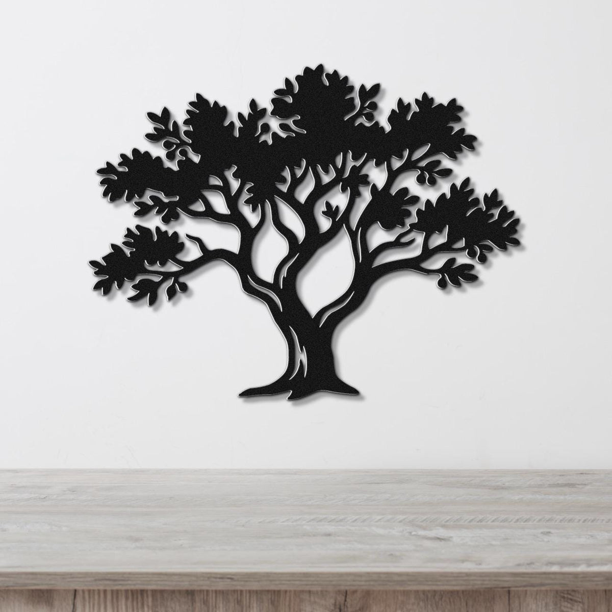 Black metal tree wall art with leaf and branch cutouts, mounted on a white wall above a light wood counter.