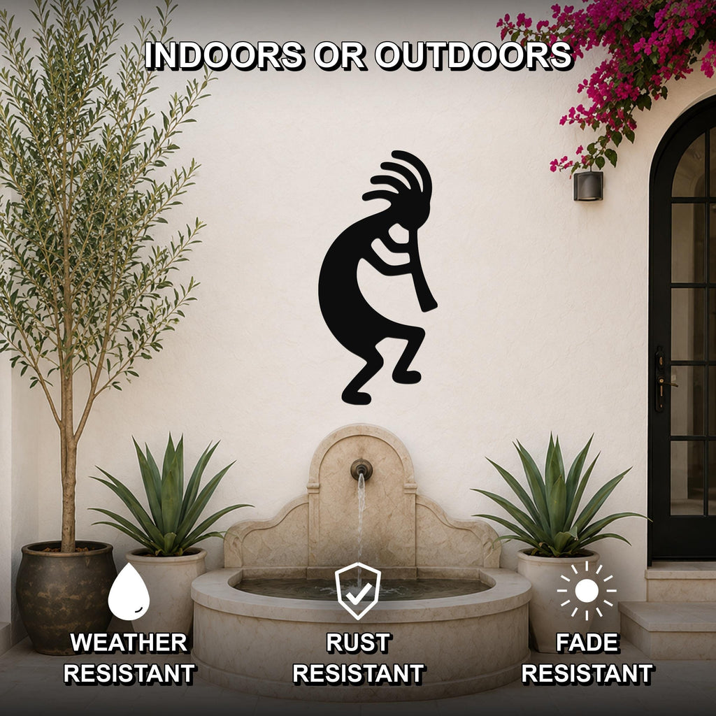 Black metal Kokopelli wall art silhouette with feathered headdress and flute, mounted on an outdoor patio wall above a stone fountain, flanked by potted plants.