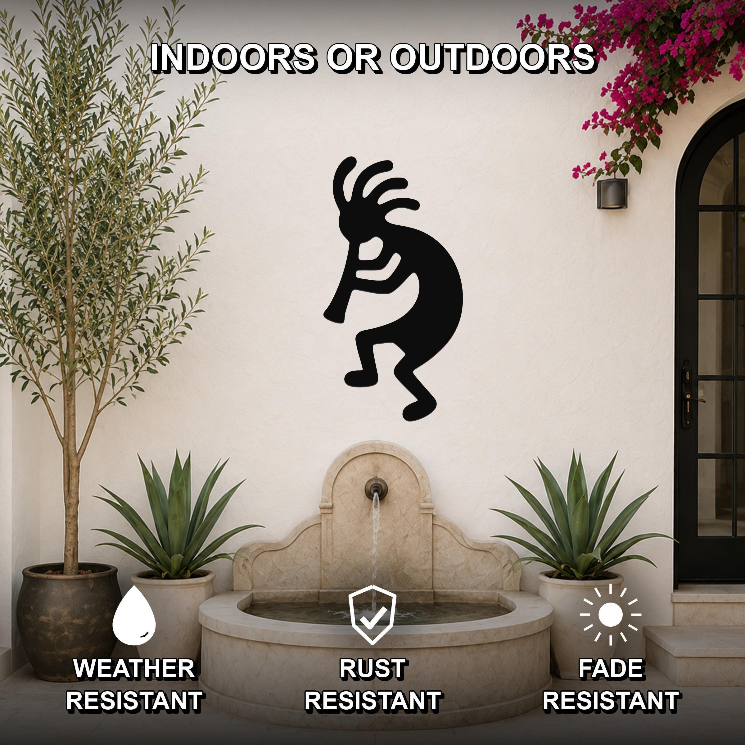 Black metal Kokopelli wall art silhouette mounted on an outdoor wall above a stone fountain, flanked by potted plants and a flowering vine.