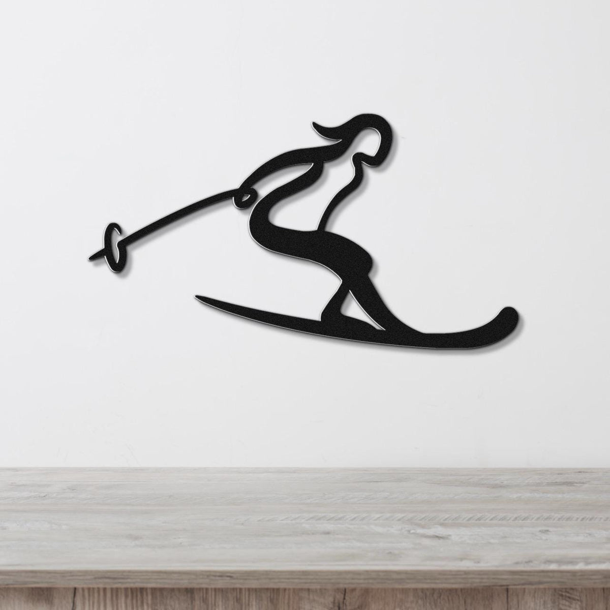 Black metal wall art of a skier silhouette with ski poles and skis, mounted on a white wall above a wooden surface.