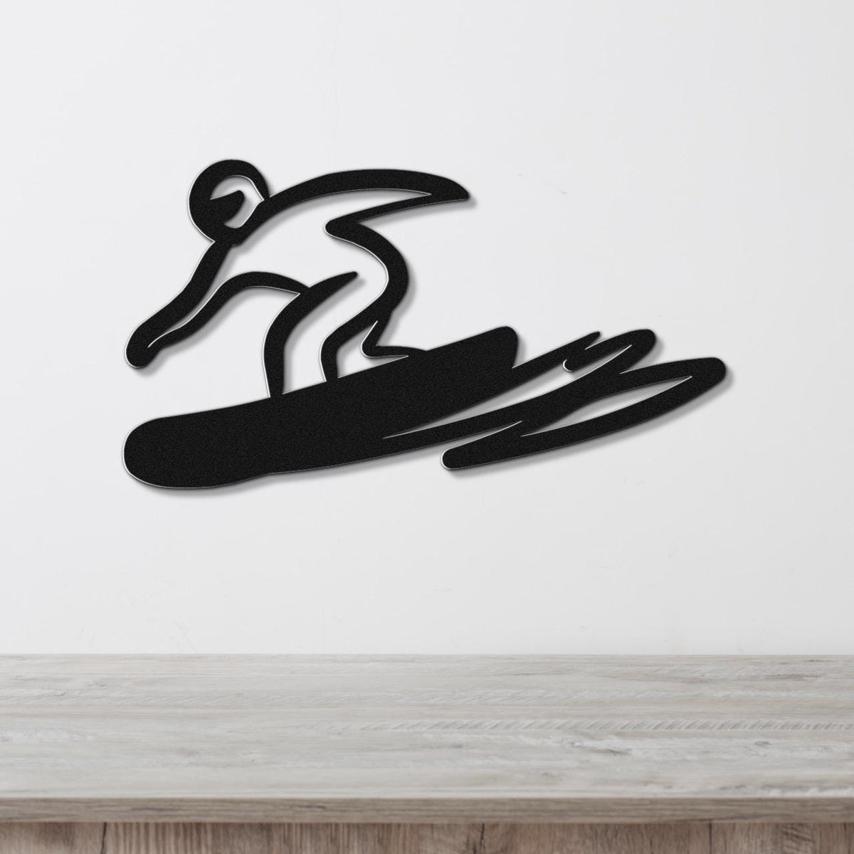 Black metal wall art featuring a bold silhouette of a snowboarder in motion, mounted on a white wall above a wooden surface.