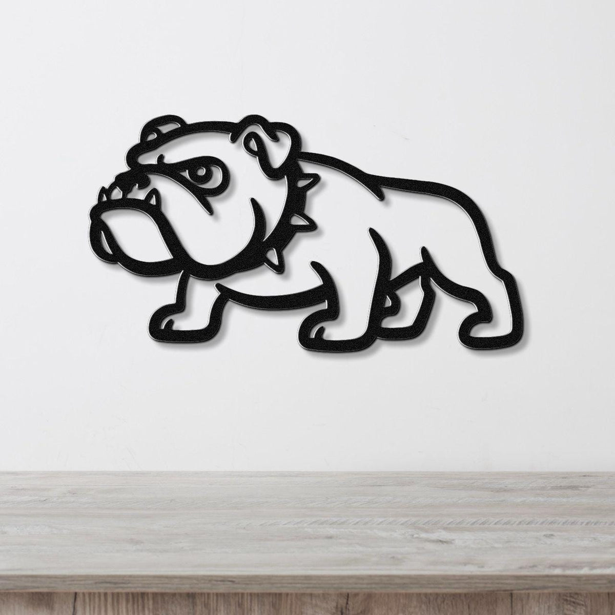 Black metal bulldog wall sculpture with bold silhouette and internal cutout details, mounted on a white wall above a light wood surface.