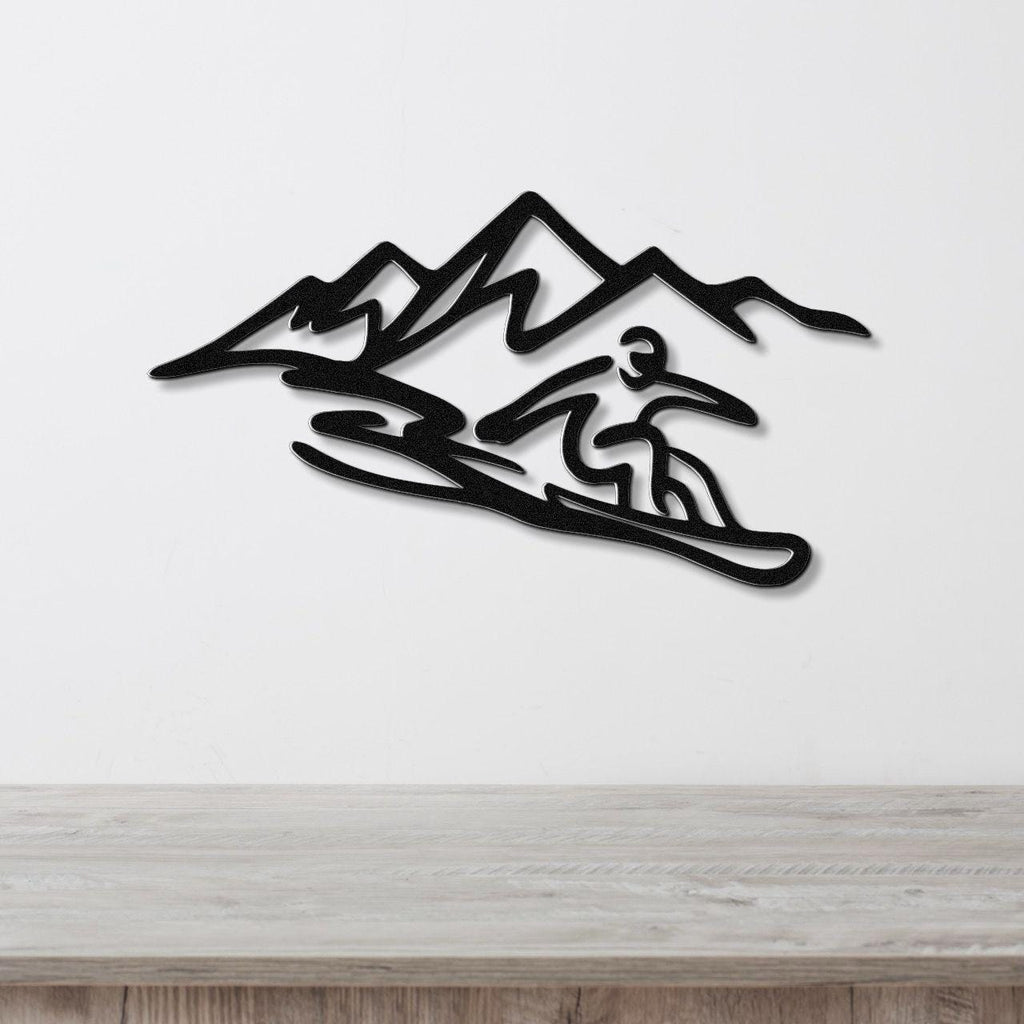Black metal wall art featuring a snowboarder silhouette in motion against a mountain range, mounted on a white wall above a wooden surface.