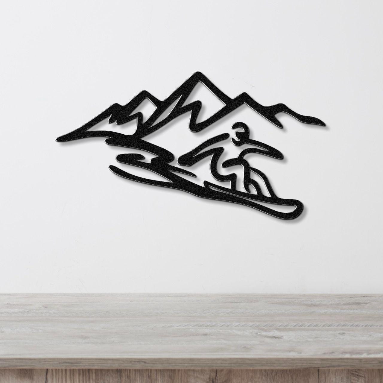 Black metal wall art featuring a snowboarder silhouette in motion against a mountain range, mounted on a white wall above a wooden surface.