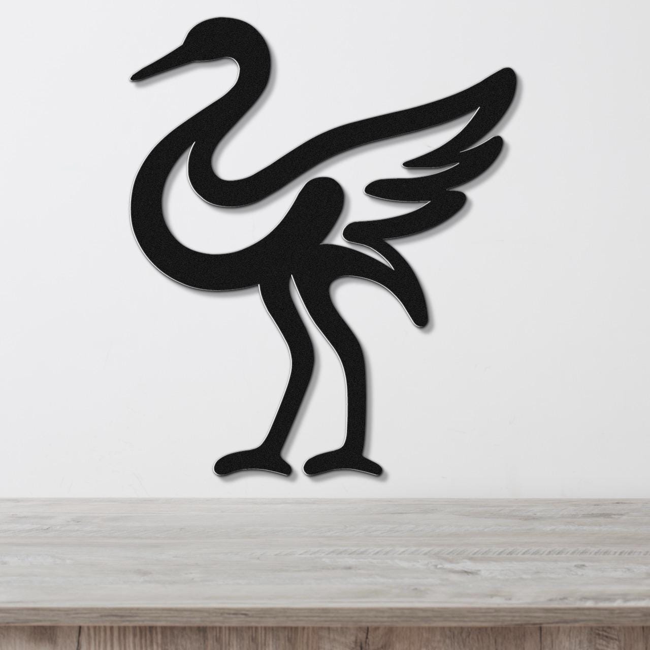 Black metal crane wall art with a minimalist silhouette design, mounted on a white wall above a light wood surface.