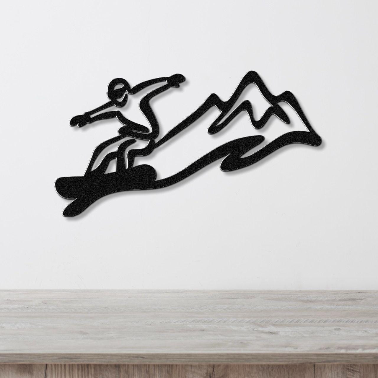 Black metal wall art featuring a snowboarder silhouette in motion above a mountain range, mounted on a white wall above a wooden counter.