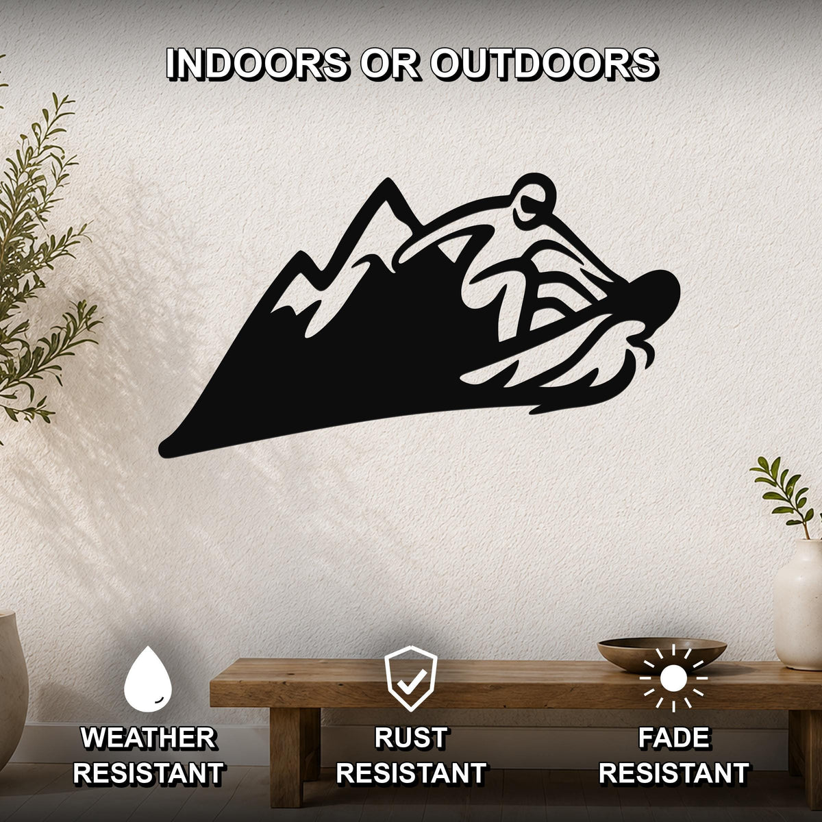Black metal wall art featuring a snowboarder silhouette cutting through mountain peaks, mounted on a textured wall above a wooden bench in a living room.